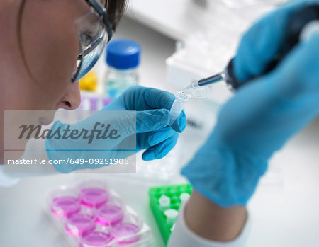 Biotechnology research, scientist pipetting sample into vial for analysis in laboratory, over shoulder view