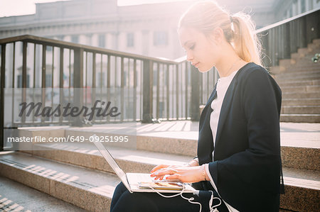 Young woman sitting on city stairway typing on laptop