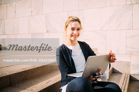 Young woman sitting on city stairway with laptop, portrait