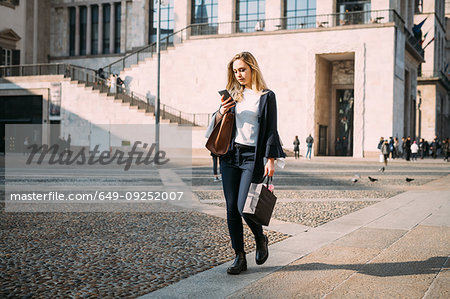 Young woman strolling in city square looking at smartphone