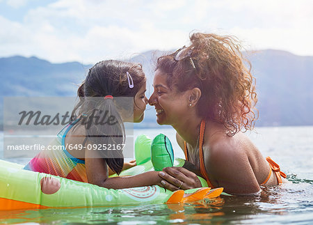 Mother rubbing noses with daughter on inflatable frog in lake
