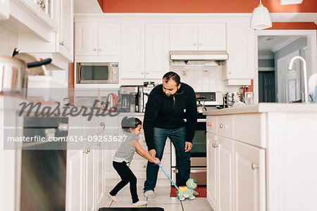 Girl playing with push toy in kitchen, father watching