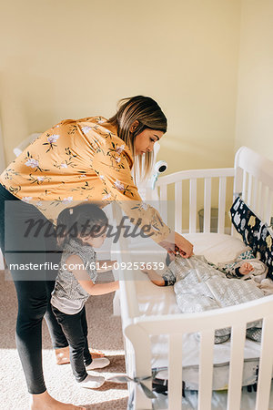 Girl and mother putting baby brother in crib