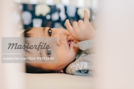 Baby boy lying awake and sucking thumb in crib, close up portrait