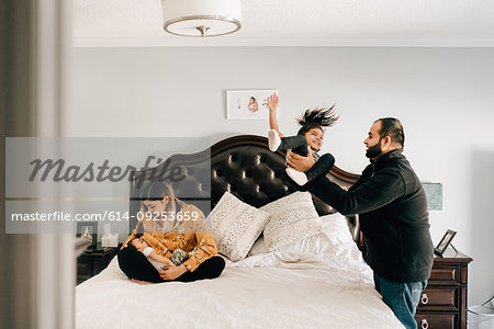 Girl being thrown onto bed by father, next to mother nursing baby brother