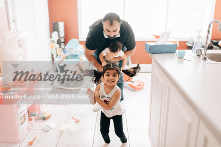 Girl playing in kitchen in front of father and baby brother, portrait