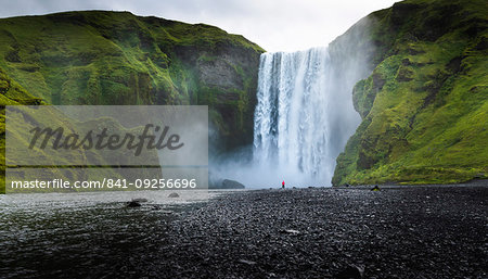 Visitor dwarfed by plunging waters of Skogafoss, Iceland's most iconic waterfall, situated on the Skoga River, Southern Region, Iceland, Polar Regions