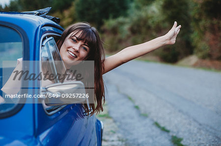 Woman driving, sticking head and arm out of car window