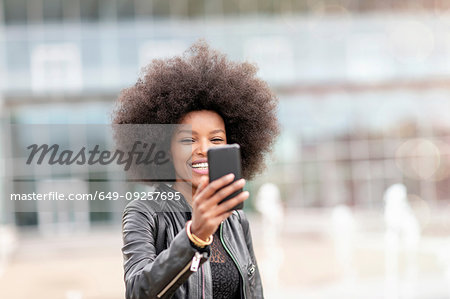 Young woman with afro hair taking smartphone selfie on city concourse