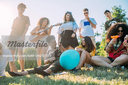 Group of friends relaxing, playing guitar at picnic in park