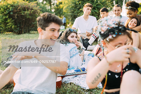 Group of friends watching man playing with confetti at picnic in park