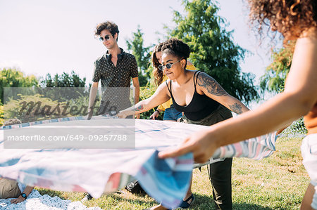 Friends laying picnic blanket in park