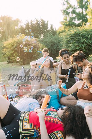 Group of friends relaxing, blowing bubbles at picnic in park