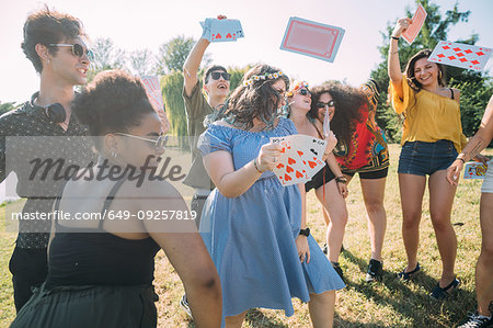 Group of friends dancing, throwing playing cards into air in park