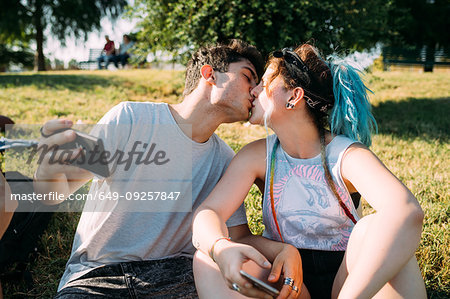 Couple kissing, using smartphone in park