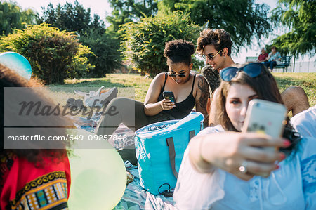 Group of friends relaxing, taking selfie at picnic in park