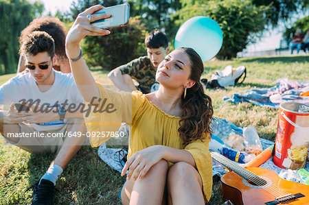 Group of friends relaxing, taking selfie at picnic in park