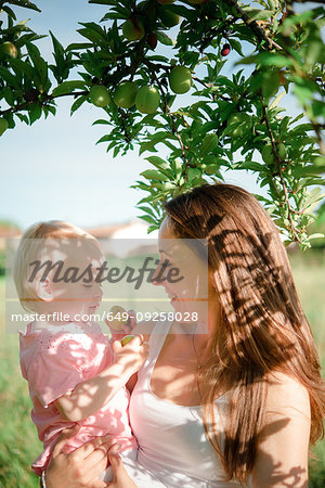 Mother gazing at toddler daughter under fruit tree, Arezzo, Tuscany, Italy