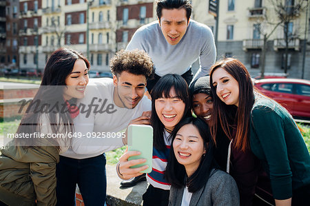 Young male and female adult friends taking smartphone selfie near city street