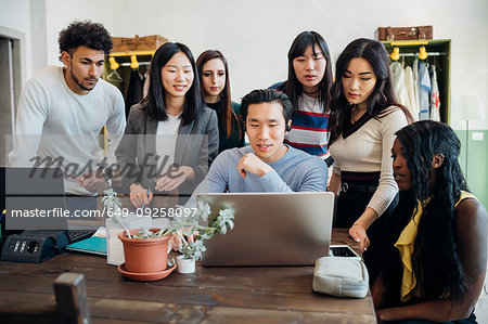 Group of young businessmen and women looking at laptop in office meeting