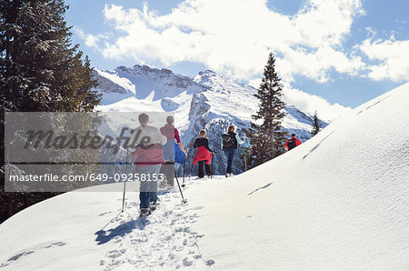 Mature couple and daughters snowshoeing in snow covered mountain landscape, rear view, Styria, Tyrol, Austria
