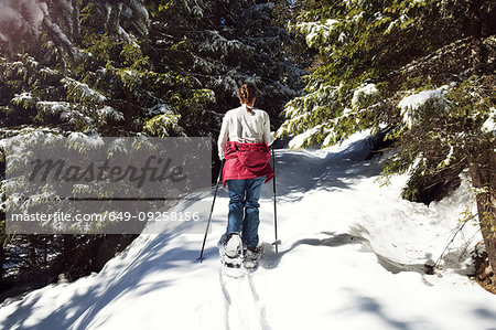 Teenage girl snowshoeing in snow covered mountain forest, rear view, Styria, Tyrol, Austria