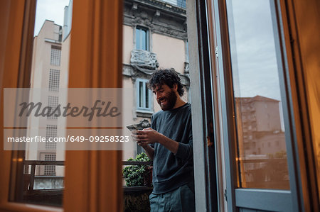Bearded young man using smartphone on balcony