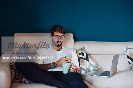 Mid adult man reclining on sofa looking at smartphone