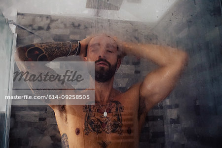 Mid adult man with tattooed chest in shower