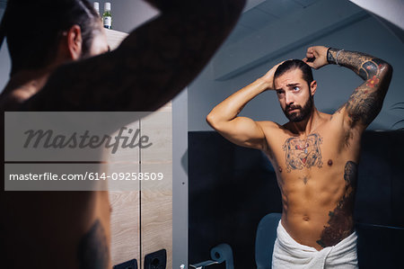 Mid adult man with tattoos combing hair at bathroom mirror, mirror image