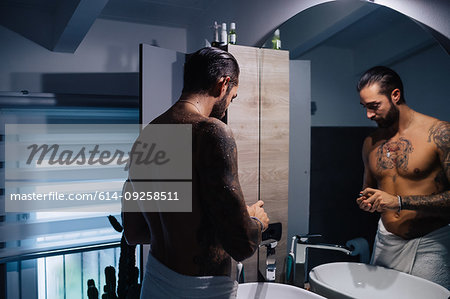Mid adult man with tattoos getting ready at bathroom mirror