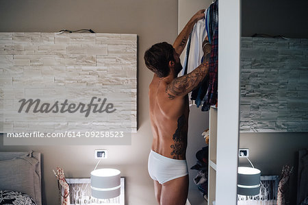 Mid adult man with tattoos selecting shirt from wardrobe