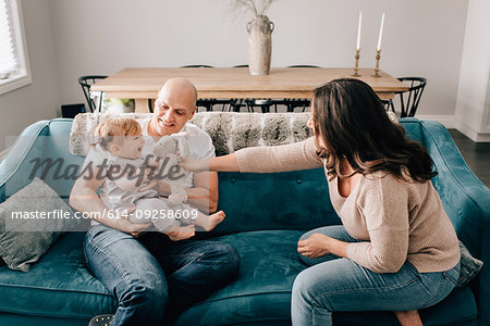 Mother and father on sofa with baby daughter playing with soft toy