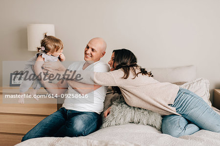 Mother and father on bed lifting up baby daughter