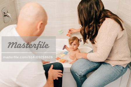 Mother and father playing with baby daughter in bath, over shoulder view