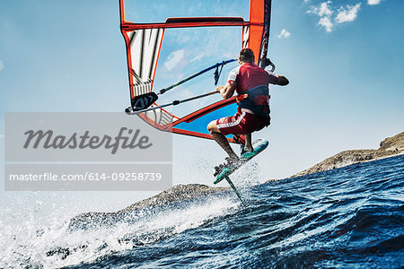 Young man mid air windsurfing ocean waves, side view, Limnos, Khios, Greece