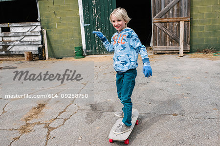 Blond boy skateboarding in farmyard