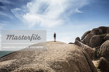 Young woman practicing yoga taking a break standing on top of beach boulder, Cape Town, Western Cape, South Africa