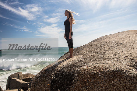 Young woman practicing yoga taking a break looking out from beach boulder, Cape Town, Western Cape, South Africa
