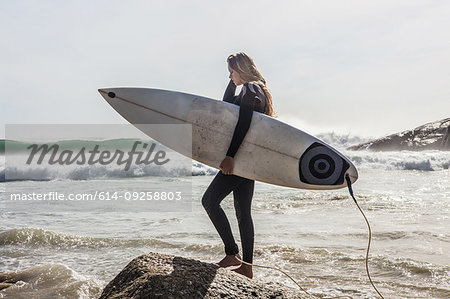 Young female surfer stepping onto beach rock, Cape Town, Western Cape, South Africa