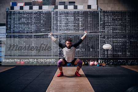 Young man lifting weight bar in gym