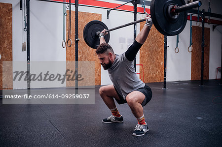 Young man squatting and lifting barbell in gym
