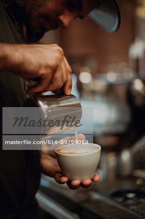 Barista pouring milk into cup of latte in cafe, close up of hands