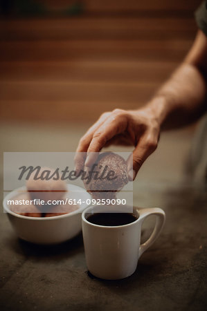 Man dipping doughnut into black coffee at cafe table, cropped shallow focus