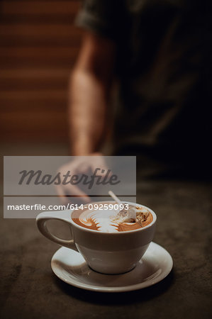 Barista at cafe counter with cup of mocha topped with toasted marshmallow, cropped shallow focus