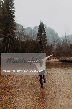 Young woman jumping in river shallows, rear view, Yosemite Village, California, USA