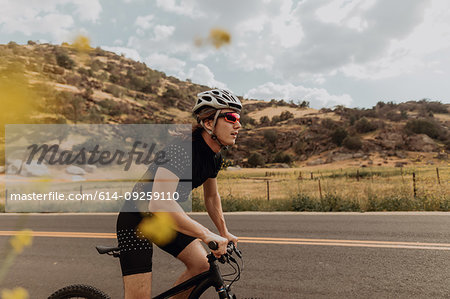 Young male cyclist cycling on rural road, side view, Exeter, California, USA