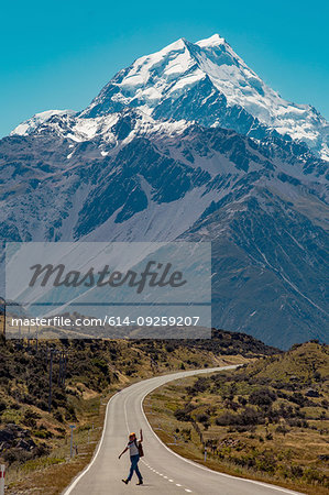 Hiker crossing road leading towards mountains, Wanaka, Taranaki, New Zealand