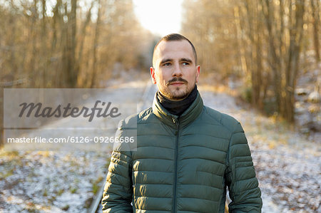 Young man wearing green puffer jacket on snowy road through forest