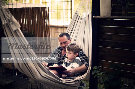 Mid adult man and boy reading in hammock